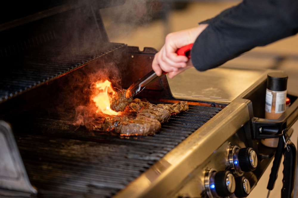 Imagen de una parrilla con unas manos cocinando trozos de ternera