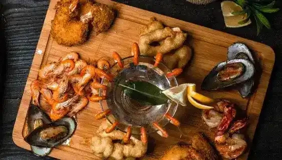 Foto de una tabla de mandera sobre la cual hay diversas de marisco y una foto de tres atunes recién pescados metidos en una caja