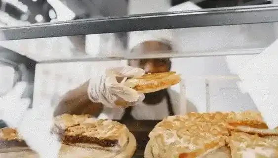 Foto de unas manos amasando y un dependiente tomando un trozo de tarta del mostrador